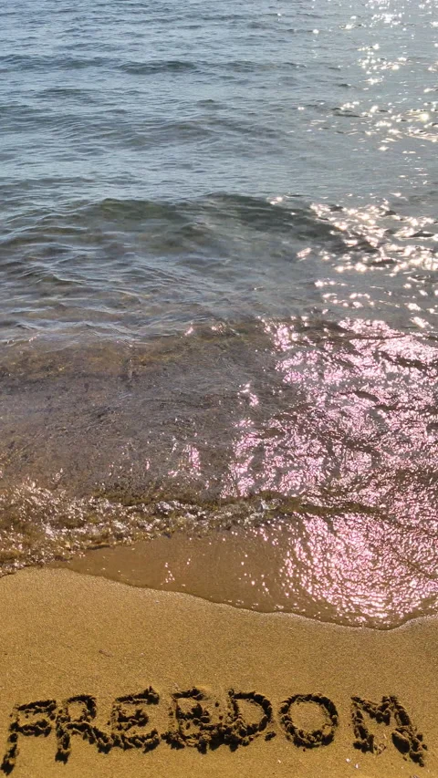 Vertical freedom text written on beach sand in slow motion Video stock 335758298