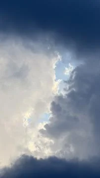 Vertical gap in heavy dark storm clouds revealing soft white illuminated clouds Stock Photos