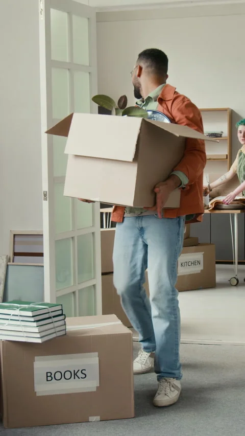 Vertical of Gen Z Guy Carrying Box into Room and Tripping over Another One Stock Footage 323298425