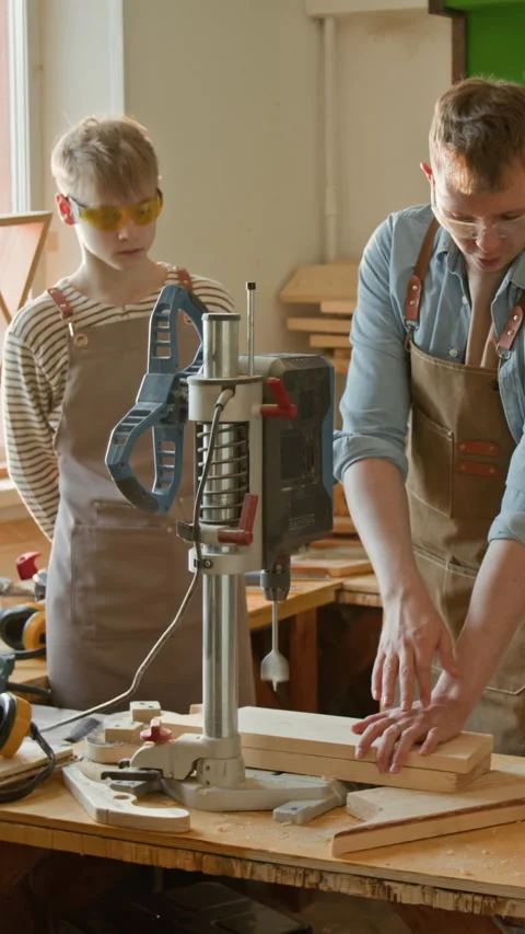 Vertical of Gen Z Woodworker Teaching Teenage Boy to Operate Drilling Machine Stock Footage 334419112