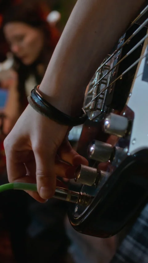Vertical of Girl Plugging Audio Cable into Bass Guitar and Adjusting Knobs Stock-Footage 342813851
