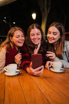 Vertical. Girls having fun using a smartphone sitting on a terrace at the Stock Photos
