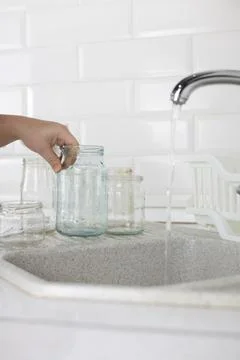 Vertical. Glass sorting. In the kitchen sink, a woman under the tap washes a Stock Photos