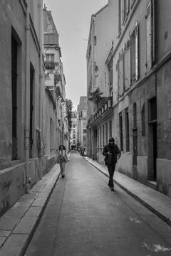 Vertical grayscale of people walking down a narrow street in Paris Stock Photos