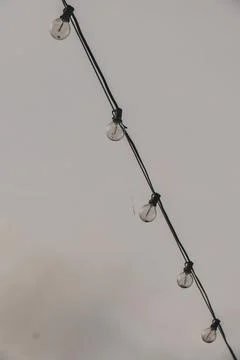Vertical grayscale shot of string lights against a cloudy sky Stock Photos