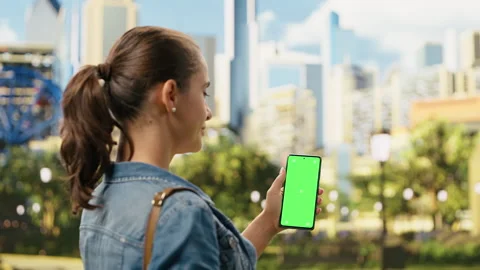 Vertical green screen mockup on phone held by casual woman in city park Stock Footage 343500473