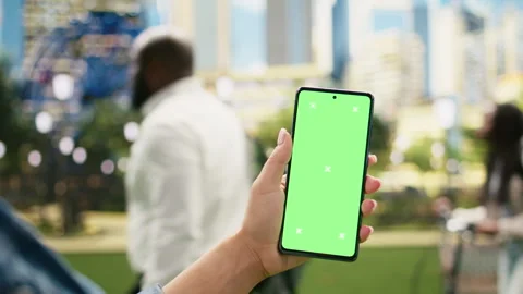 Vertical green screen mockup on phone held by casual woman in city park Stock Footage 343506447