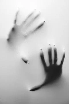 A vertical greyscale shot of a person's hands behind a frozen glass - fear an Fotos de archivo