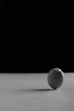 Vertical of a half-peeled egg on a table in black and white. Stock Photos