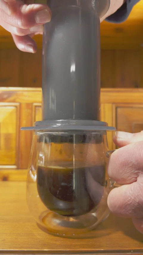 Vertical - A hand pushing brewed coffee down a chamber into a glass mug. Video stock 293777765