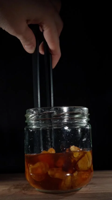 Vertical Hand Stirring Fermented Garlic Honey Jar with Tweezers Slow Motion Stock Footage 324920584
