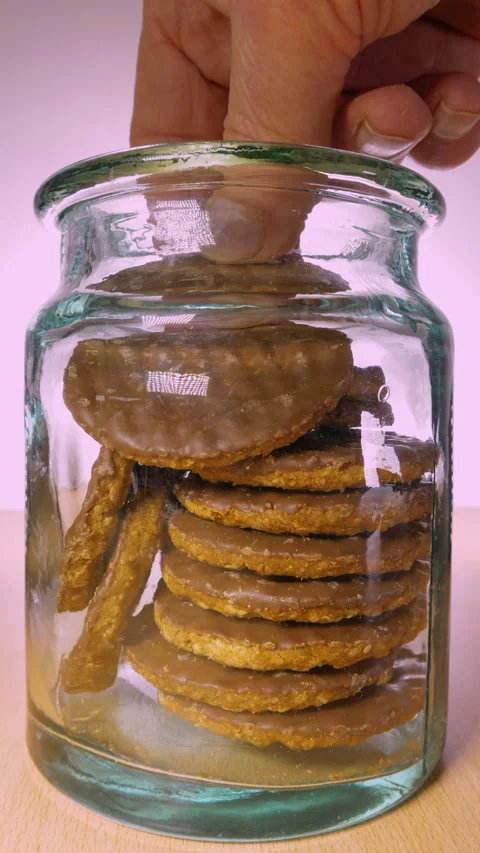 Vertical - A hand taking a chocolate coated digestive biscuit from a glass jar. Video stock 280229342