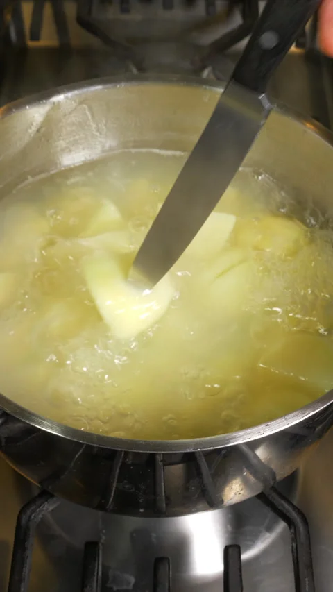 Vertical - A hand using a knife to see if boiling potatoes in a pan are cooked. Stock Footage 282471763