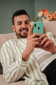 Vertical. Handsome young man using a mobile phone lying on a sofa at his living Stock Photos