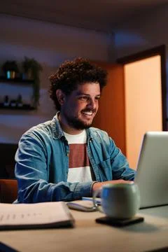 Vertical. Happy freelancer man working at home with laptop on a desk at night Stock Photos
