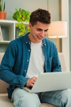 Vertical. Happy freelancer man working at home with a laptop on a sofa. Young Stock Photos