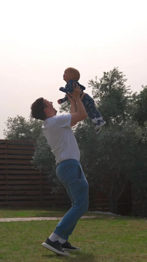 Vertical of Happy man throws up and catches little boy in backyard Stock Footage 275670923