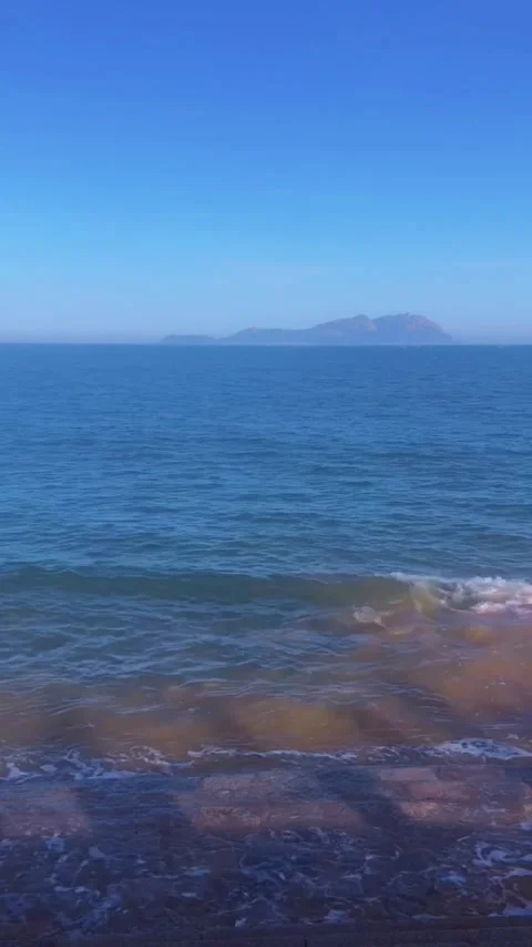 Vertical HD footage of clear blue ocean waves gently rolling onto a rocky shore Vidéo 333605097