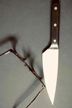 A vertical high angle shot of a sharp knife next to a brown eyeglasses on a g Foto stock