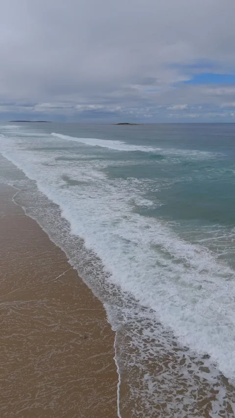 Vertical high-angle of turquoise waves breaking on a golden sand beach. Vídeo Stock 332542543