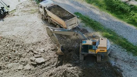 Vertical high angle view of an excavator digging dirt next to a dump truck. Stock Photos
