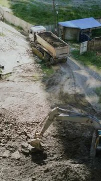 Vertical high angle view of an excavator digging dirt next to a dump truck. Stock Photos