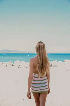 Vertical image of blonde long-haired woman walking on the beach in sunny day. Stock Photos