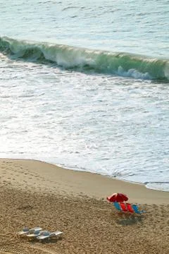 Vertical image of empty beach with chairs and parasol and the crashing waves Stock Photos