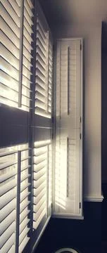 Vertical image of light shining through window with plantation shutters Stock Photos