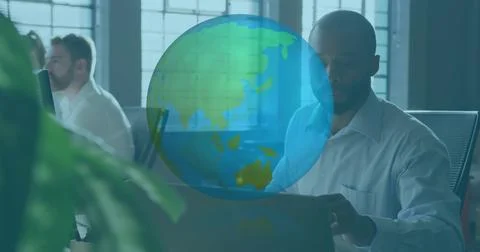 Vertical image: Man typing at laptop in IT dim globe emerging over desk rotating Stock Photos