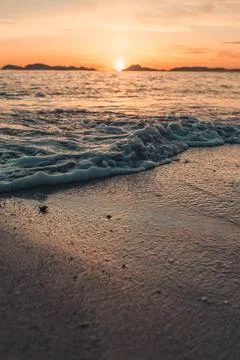 Vertical image of a tide on the beach over the sand during a colorful sunse.. Photos