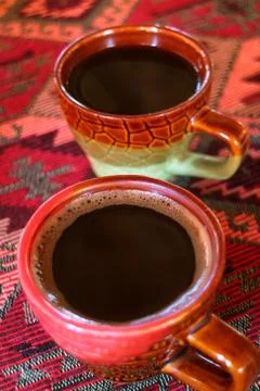 Vertical image of two cups of hot coffee on the ethnic pattern table cloth Foto stock