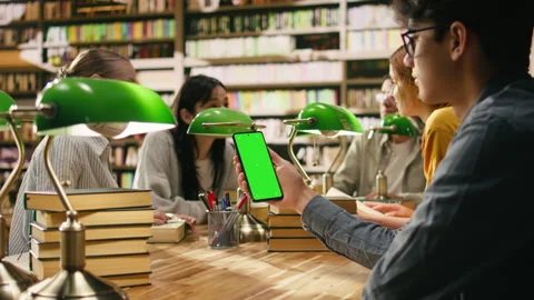 Vertical isolated green screen on smartphone held over wooden library desk Stock Footage 336359559