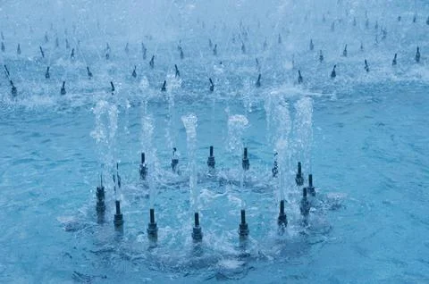Vertical jets of water form a circle. Turquoise water of the city park founta Stock Photos