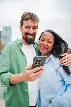 Vertical. Joyful couple happily using a smartphone while sharing a delightf.. Stock Photos