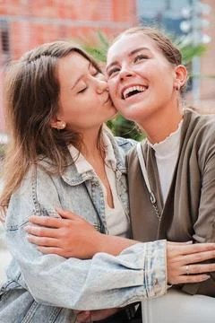 Vertical. Joyful moment of affection between two female friends as one gives a Stock Photos