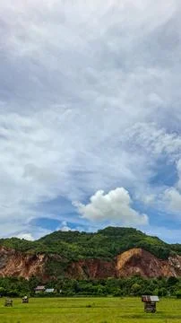 Vertical landscape of green rice fields and rocky cliff hills under cloudy sky Stock Photos