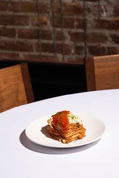 Vertical lasagna slice and red sauce on white plate white tablecloth Stock Photos