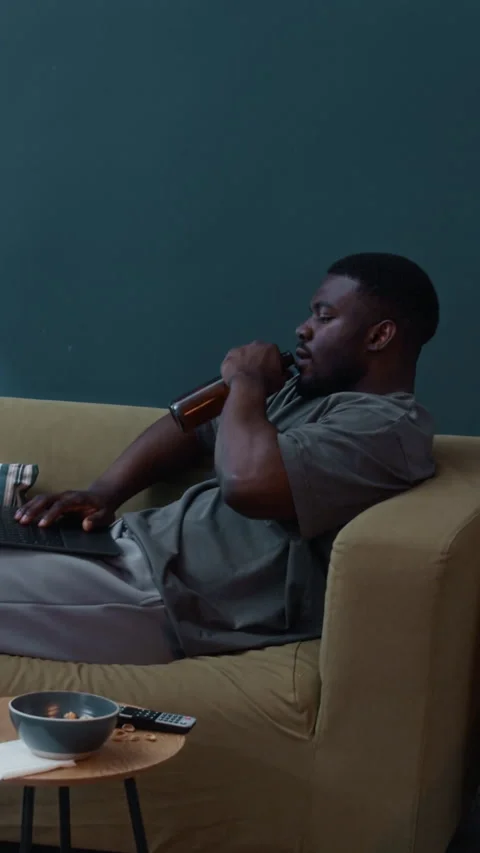 Vertical of Lonely Man Under House Arrest Drinking Beer while Looking at Laptop Stock Footage 313927489