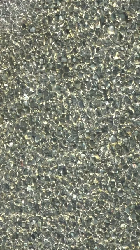 Vertical loop of clear water ripples and shimmering sunlight on pebbles Video stock 332701667