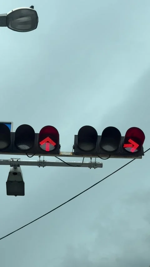 Vertical Low Angle Shot Of Flickering Red LED Traffic Light Arrows Under Overcas Stock Footage 343725515