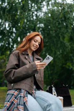 Vertical low-angle shot of positive young woman with long red hair using her Stock Photos