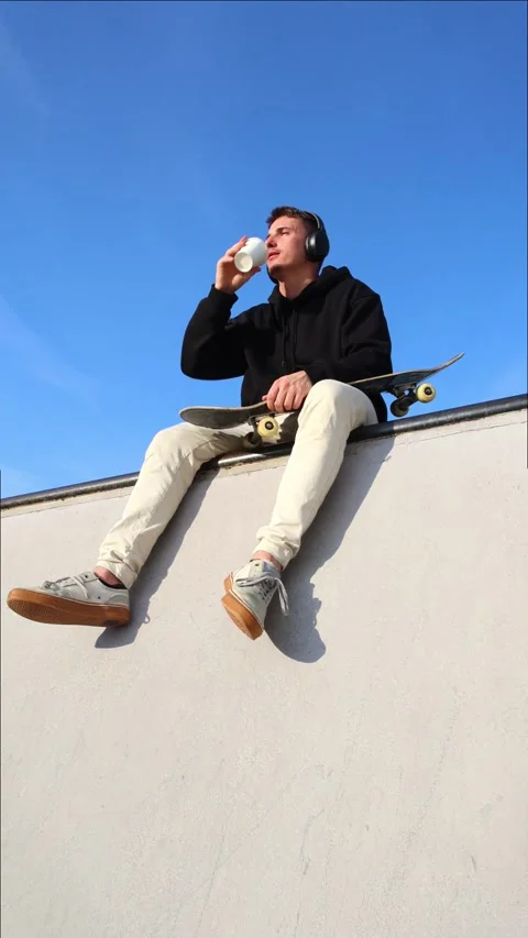 Vertical Low-Angle Shot of a Skater Drinking Coffee While Listening to Musi.. Stock Footage 285766140