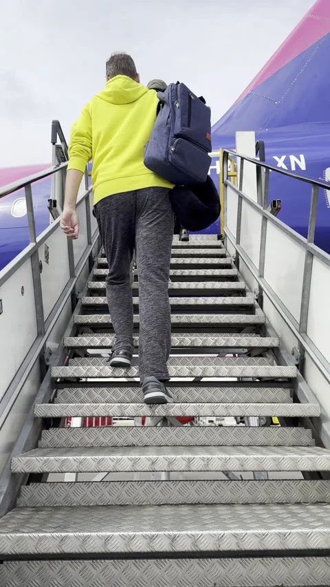 Vertical low angle tracking shot of man walking up airplane stairs for boarding Stock Footage 336495765