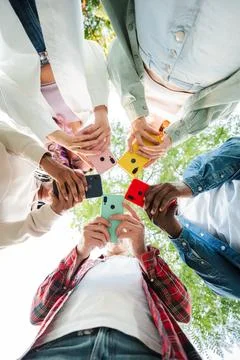 Vertical low angle view of group of friends standing in circle, all using c.. Stock Photos