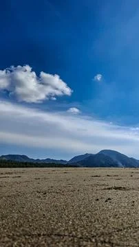 Vertical low angle view of sandy beach with mountains and blue sky Stock Photos