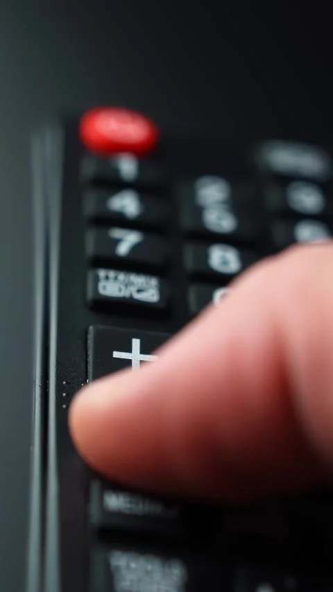 Vertical macro close-up of a finger pressing volume down on a TV remote Stock-Footage 329488536