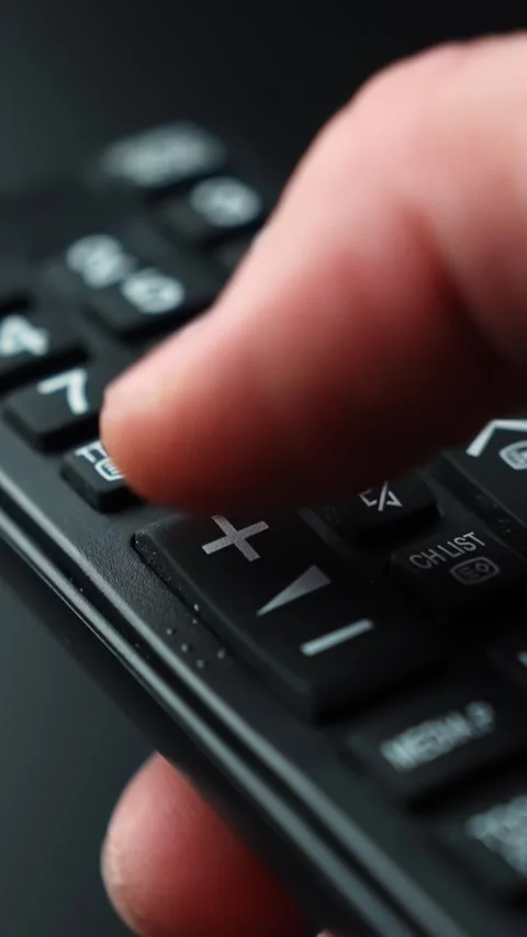 Vertical macro close-up of a finger pressing the plus key on a TV remote to Stock Footage 331318646