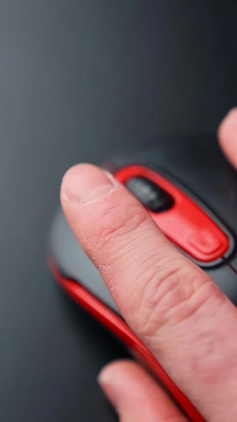 Vertical macro of a finger clicking a red and black computer mouse on a dark Stock Footage 329479475