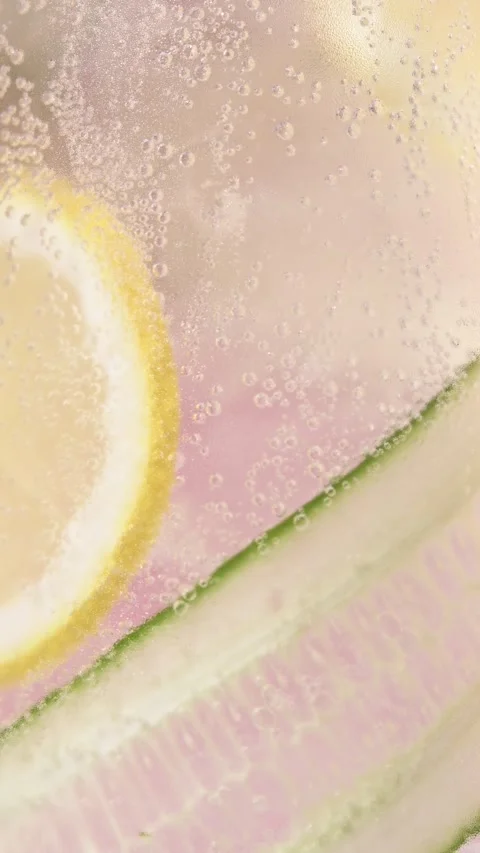 Vertical macro rotation highlights lemon and cucumber slices in sparkling soda, Stock Footage 332468337